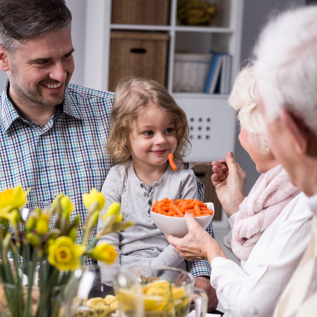 Grandmother feeding her granddaughter healthy carrots
