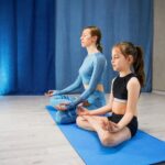 mother and daughter doing yoga together, sitting in a lotus position on a yoga mat,