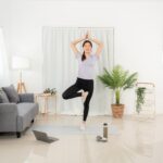 woman is watching yoga lesson online on laptop to doing with vrksasana or tree pose while workout