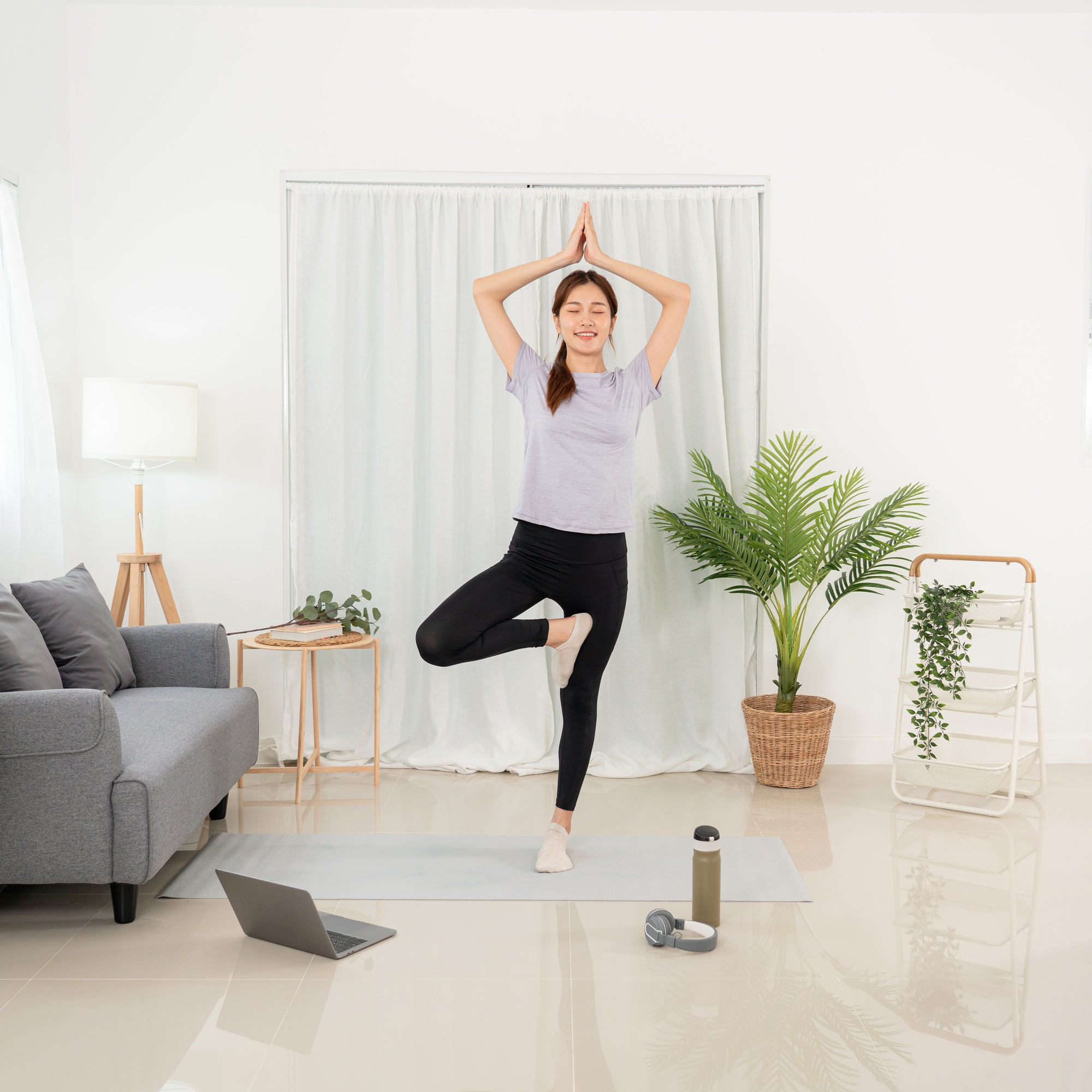 woman is watching yoga lesson online on laptop to doing with vrksasana or tree pose while workout